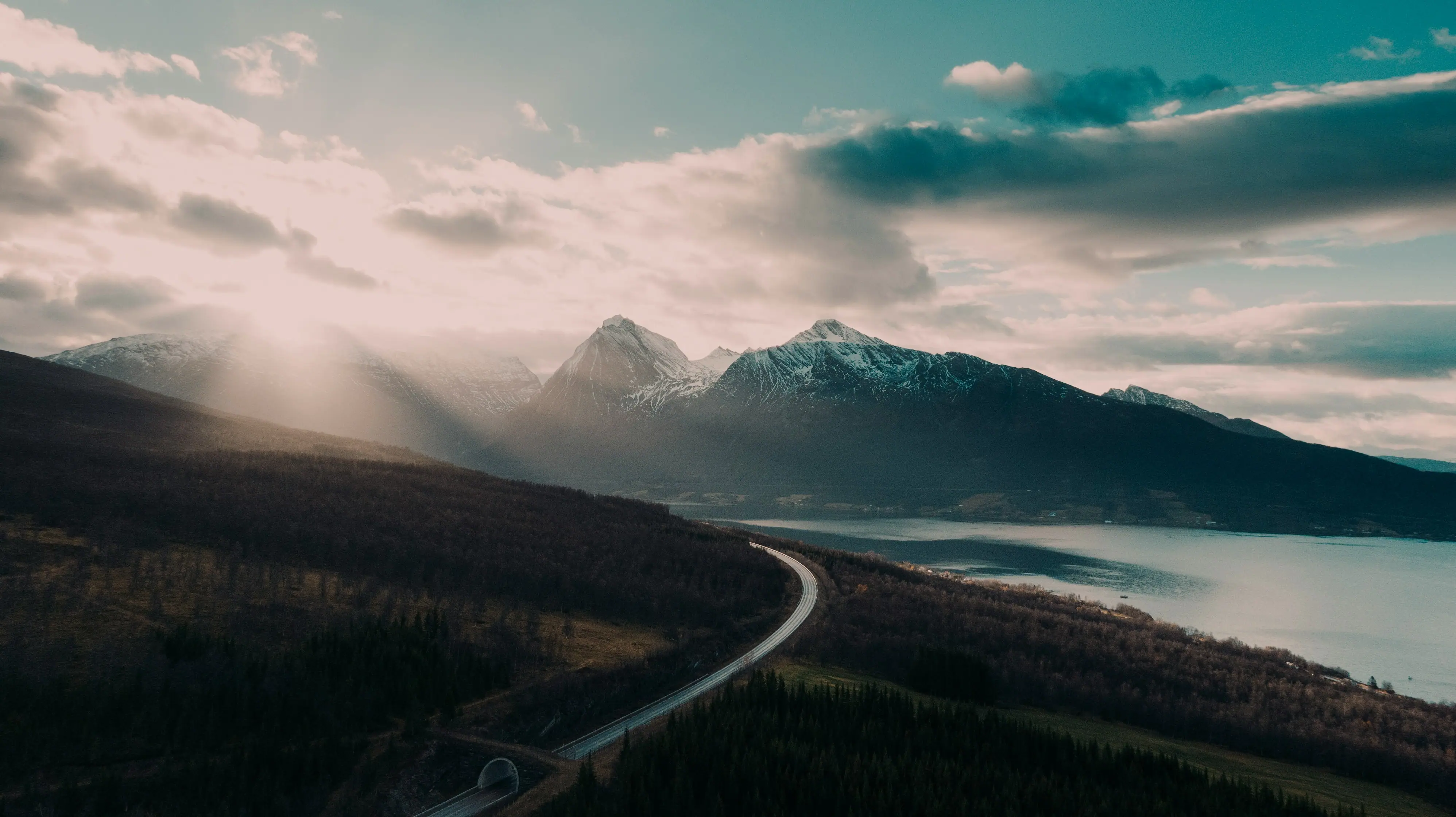 Road leading toward snow-capped fjord mountains under sunbeams